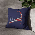 A navy blue throw pillow featuring a map-shaped graphic filled with an American flag pattern, resting on a textured gray fabric sofa.