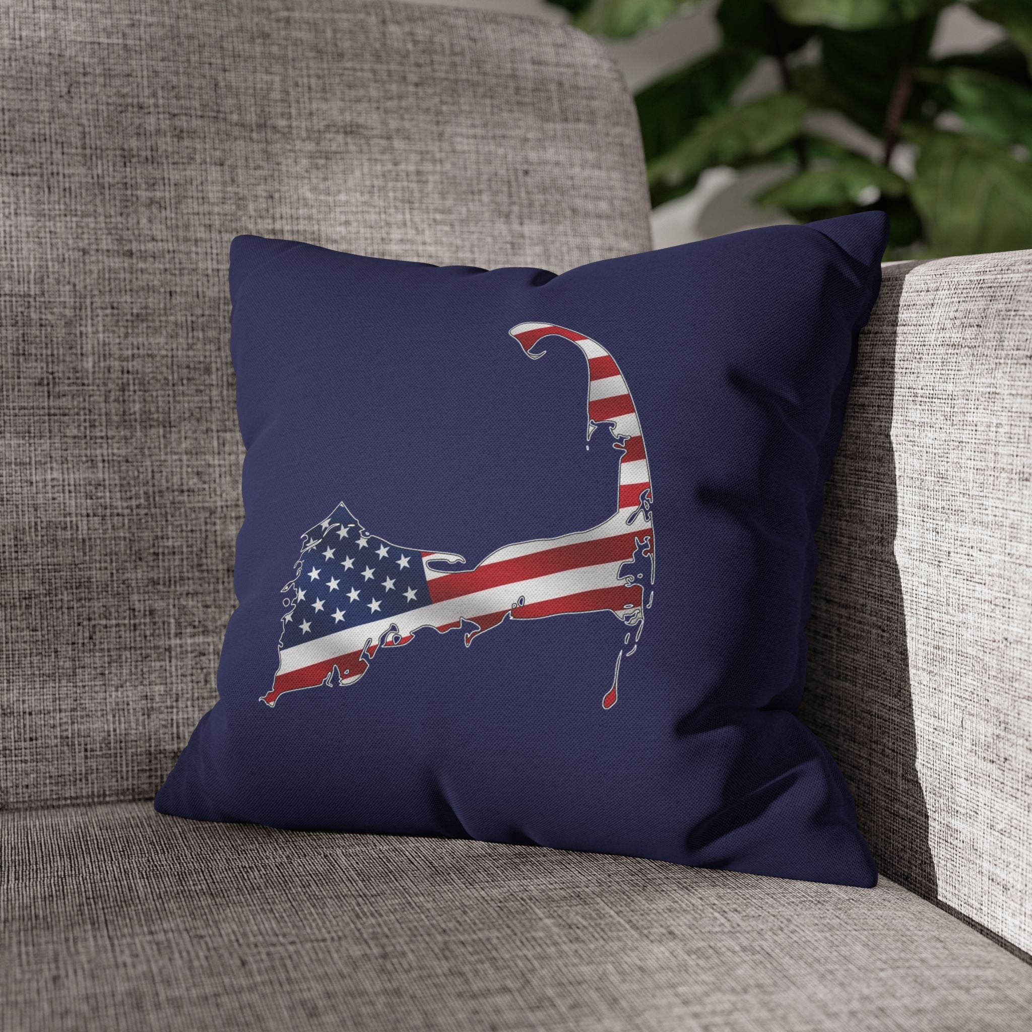 A navy blue throw pillow featuring a map-shaped graphic filled with an American flag pattern, resting on a textured gray fabric sofa.